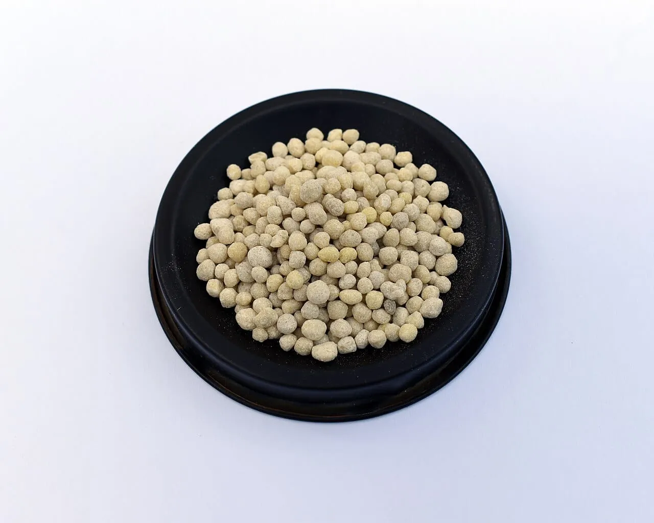 Granular fertiliser pellets, pale brown and irregular, in a shallow dish.