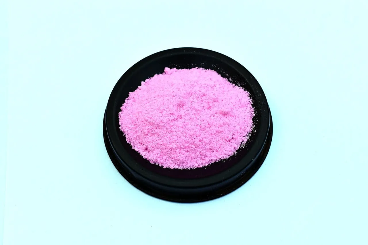 A mound of bright pink water-soluble NPK fertiliser crystals in a shallow black dish.